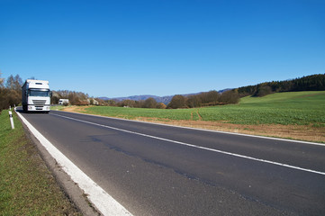White trucks arriving on the asphalt road from afar in the countryside in early spring. Flowering...