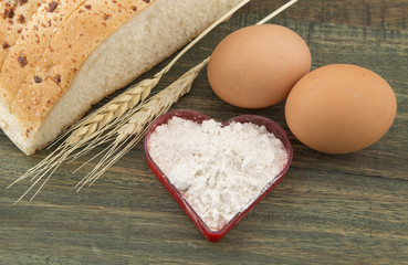 Ears of corn, bread, eggs and flour on wooden background