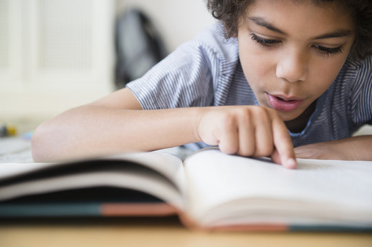 Mixed race boy reading book at desk - Powered by Adobe