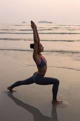 Young slim woman practicing pose from yoga on the beach at sunse