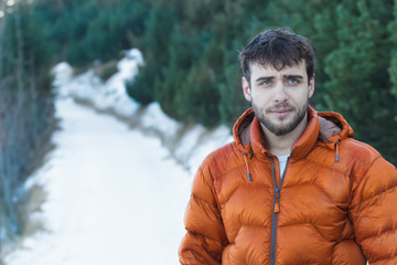 Outdoor portrait of young handsome man wearing beard and orange winter down jacket