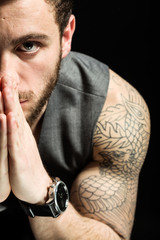 Handsome young man with tattoos thinking. Isolated on black.