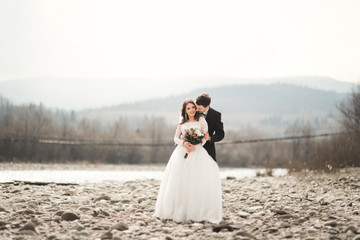 Happy wedding couple, bride and groom posing neat river against backdrop of the mountains