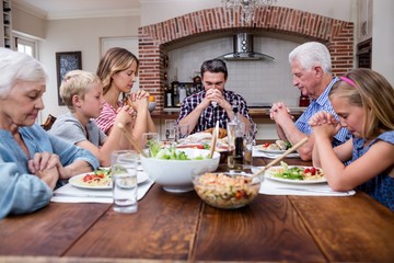 Multi-generation family praying before having meal - Powered by Adobe