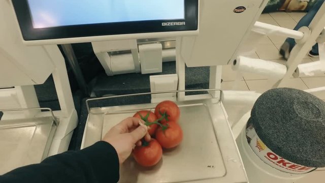 Man buying and weighing frash tomatoes in modern supermarket