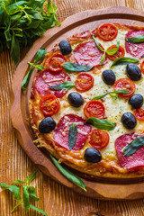Pizza with salami, black olives and tomatoes on the wooden table.