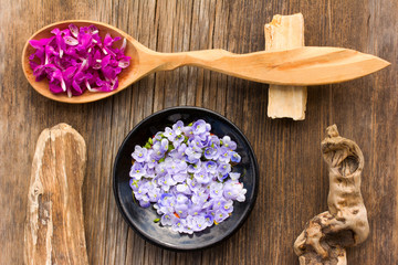 Obraz na płótnie Canvas purple flower petals plants dead-nettle in a wooden spoon and pale blue flowers Persian speedwell on an old wooden board close up. view from above. aromatherapy, herbal tea, homeopathic medicine