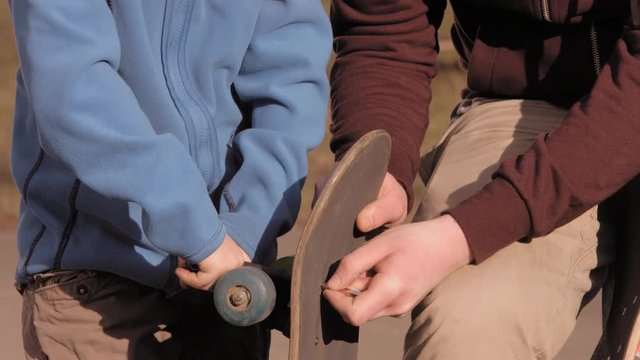little boy reparing his skateboard with his father