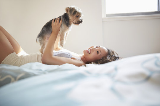 Chinese woman playing with dog on bed