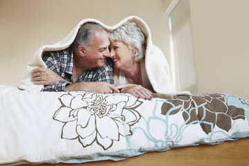 Older couple rubbing noses under blanket on bed