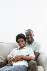 Man touching pregnant womans stomach on sofa