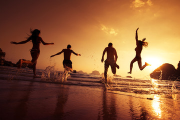 Naklejka premium Group of happy young people is running on background of sunset beach and sea