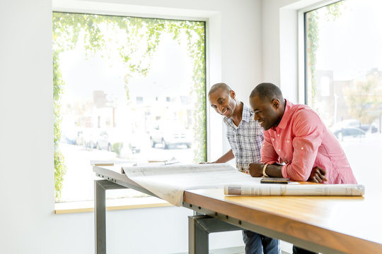 Businessmen Reading Blueprints In Office