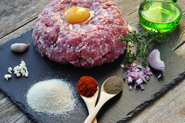 Minced meat with spices, egg and bread crumbs on a stone surface.