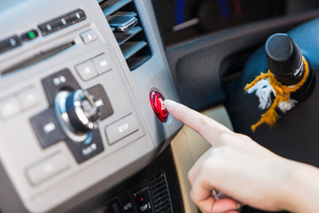 Female hand pressing emergency light button on car dashboard.