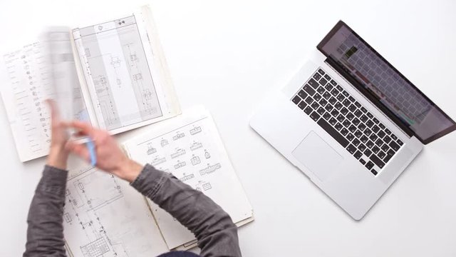 Man working at office desk with his laptop surrounded by a lot of plans. Upview