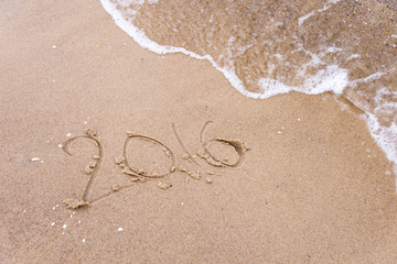 Inscription written in the wet beach sand being washed with sea water wave. Time passing away or New Year celebrating concept.