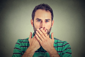 man with hands over his mouth, speechless isolated on gray wall background