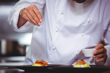 Chef sprinkling spices on dish in commercial kitchen