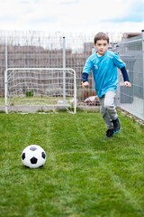 7 years boy kicking ball in the garden.