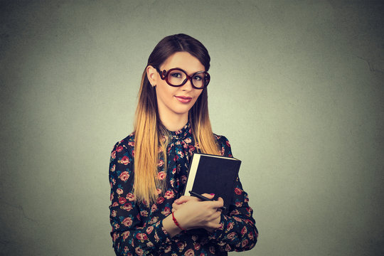 Young cheerful woman student in glasses standing and holding a book