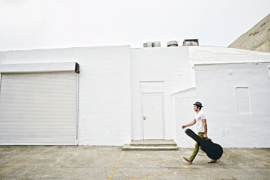 Mixed Race Musician Carrying Guitar Case On Sidewalk