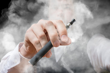 Smoking man holds electronic cigarette in hand. A lot of smoke around.
