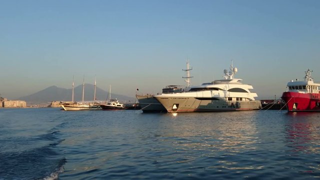 Luxury yachts docked in the port of Naples, Italy, at sunset, with view of Mount Vesuvius

