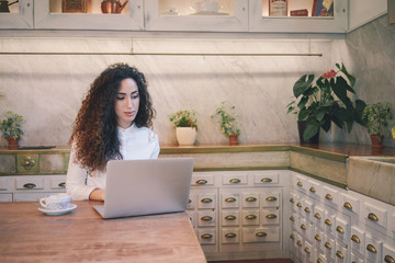 young beautiful female freelancer with long curly hair working in a cofee-shop with her laptop computer