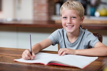 Portrait of happy boy doing homework in kitchen