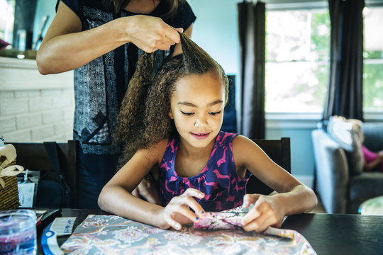 Mother Braiding Hair Of Her Daughter At Home