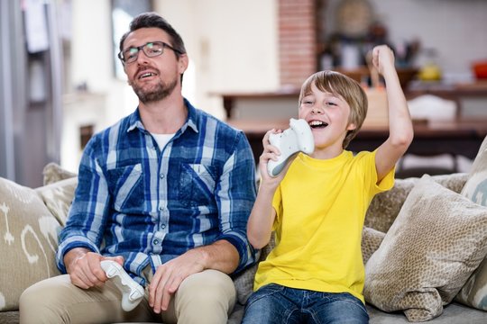 Father and son playing video game on sofa