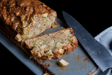 Homemade sliced apple pie and kitchen knife grey pan holder on black from high angle
