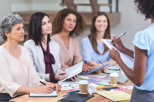 Woman noting on clipboard while colleagues listening presentation