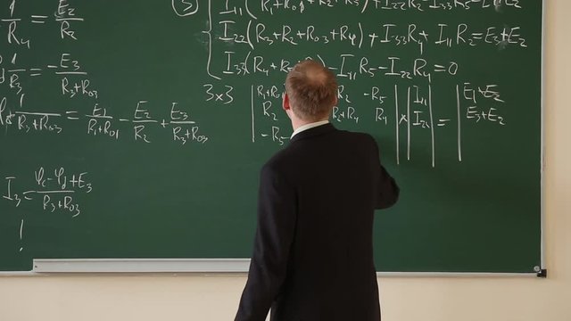 Lecturer at the university leads the lesson, he writes formulas on the blackboard
