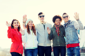 happy teenage friends waving hands on city street