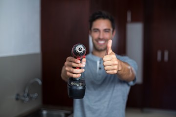 Smiling man showing thumbs up while holding cordless hand drill 