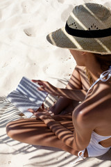 femme qui lit sur le sable à l'ombre d'une feuille de palmier © plprod