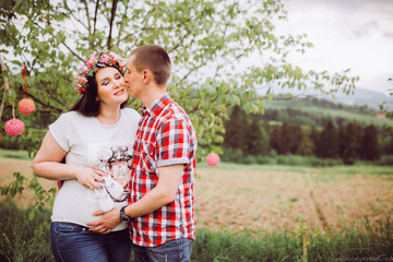 Pregnant woman in blue jeans and a T-shirt with her husband on the mountains background. Future parents