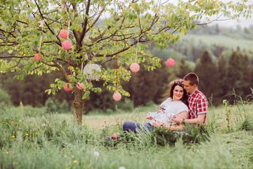 Pregnant woman in blue jeans and a T-shirt with her husband on the mountains background. Future parents