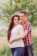 Pregnant woman in blue jeans and a T-shirt with her husband on the mountains background. Future parents