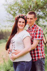 Fototapeta premium Pregnant woman in blue jeans and a T-shirt with her husband on the mountains background. Future parents