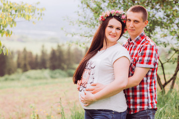 Pregnant woman in blue jeans and a T-shirt with her husband on the mountains background. Future parents
