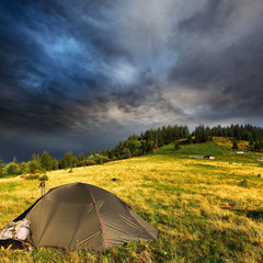 touristic tent on meadow and storm clouds