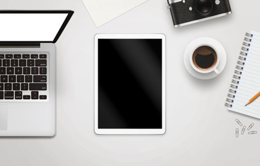 White tablet with isolated screen for mockup on office desk. Laptop, camera, cup of coffee, paper, notepad, pencil on white table. Top view.