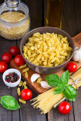 Different kinds of pasta, cherry tomatoes, basil and spices on a