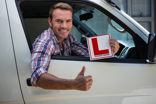 Young man gesturing thumbs up holding a learner driver sign