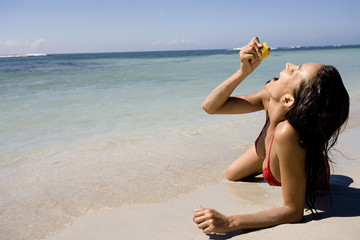 Fototapeta na wymiar femme qui mange une orange allongée sur le sable à la mer
