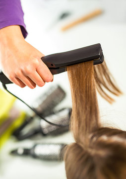Close-up of a hairdresser straightening long blonde hair with ha