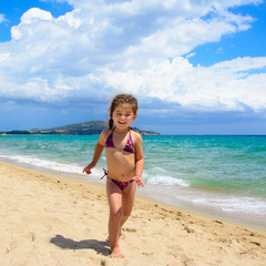 Cute little girl running on the beach in a summer day